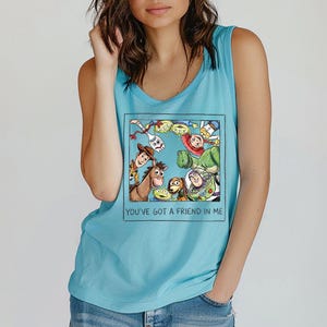 May include: A turquoise tank top with a framed graphic of Toy Story characters. The graphic includes Woody, Buzz Lightyear, and other characters. The text "YOU'VE GOT A FRIEND IN ME" is printed below the graphic.