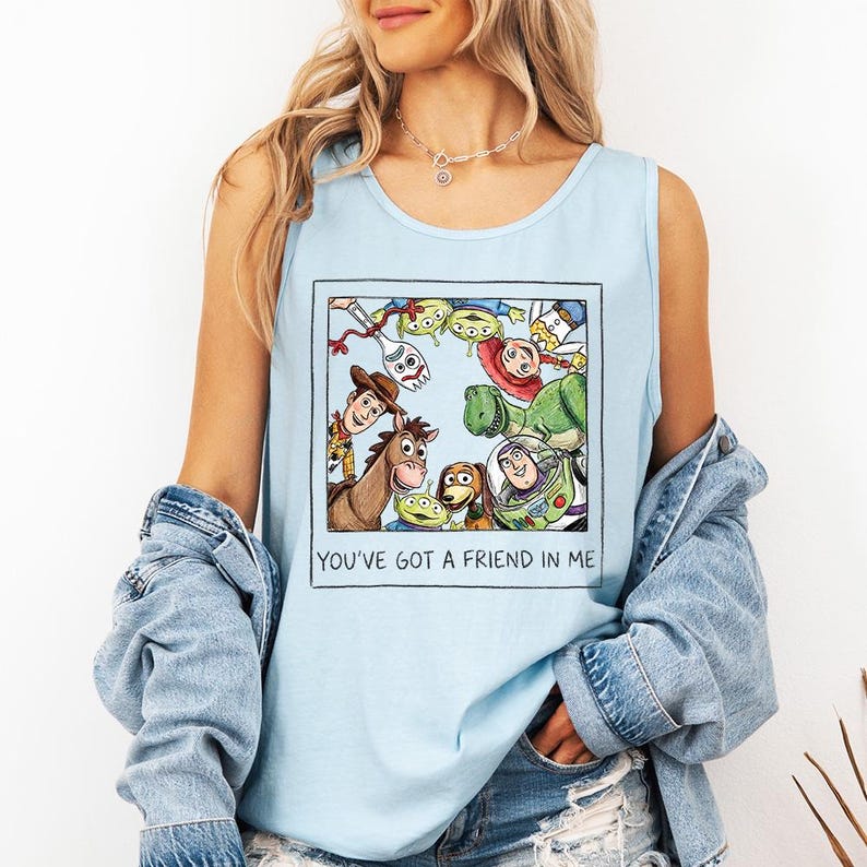 May include: Pale blue vest top with a framed illustration of Toy Story characters. The image includes Woody, Buzz Lightyear, and other characters. The text "YOU'VE GOT A FRIEND IN ME" is printed below the illustration.