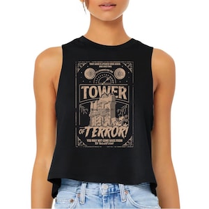Op de afbeelding: Zwarte crop top met een vintage design. Het ontwerp toont de woorden "Tower of Terror!" en een illustratie van een gebouw. De tekst luidt "You may not come back from the Twilight Zone."