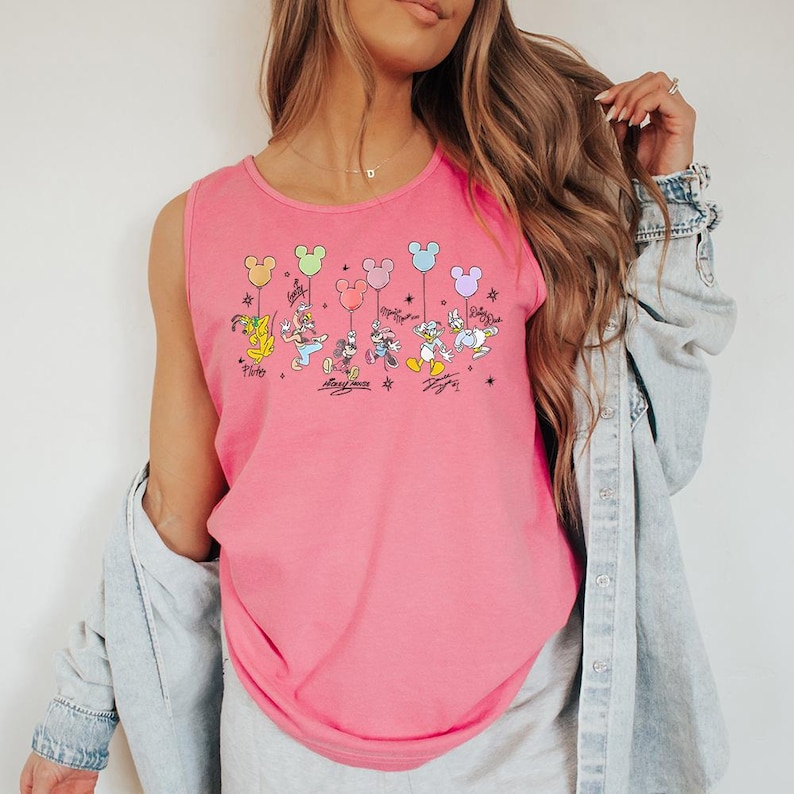 May include: Pink vest top with a cartoon graphic of Disney characters holding balloons. The characters include Pluto, Goofy, Mickey Mouse, Minnie Mouse, Donald Duck, and Daisy Duck. Each character is holding a different coloured balloon.