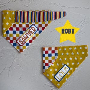 May include: Two triangular pet bandanas featuring a mustard yellow fabric with white stars and a red, white, and blue checkered pattern. One bandana displays the embroidered name Sawyer, the other Lola, and a yellow star cutout features the name Roby.