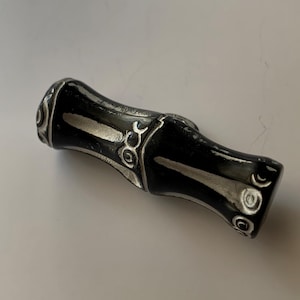 May include: A black bottle stopper with silver accents. The stopper has a bamboo-like design with decorative silver patterns around the edges. The stopper is made of a solid material and has a smooth, glossy finish.