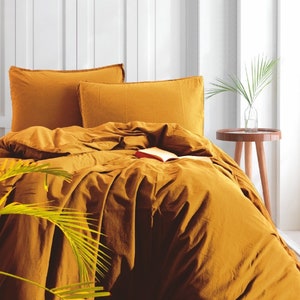 May include: A mustard yellow duvet cover and two matching pillowcases. The bedding is made of a soft, textured fabric and is arranged on a bed with a white headboard.