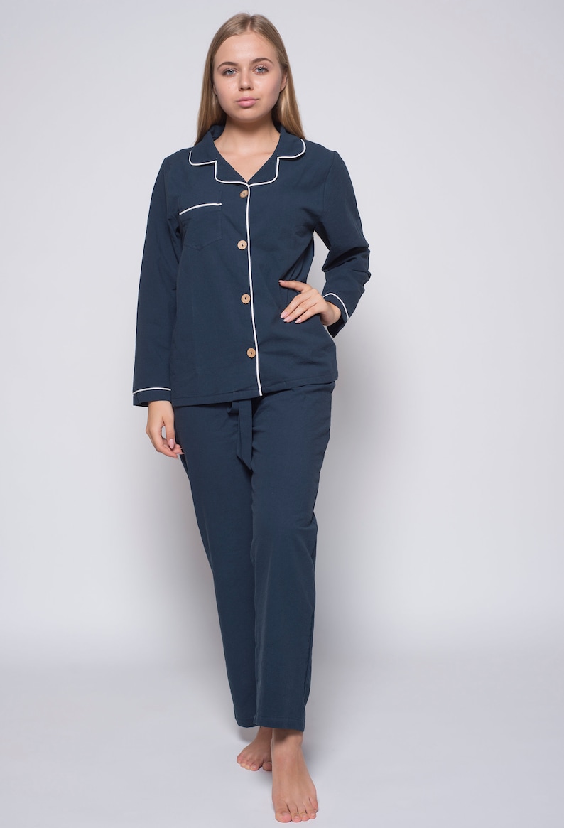 May include: A dark blue pajama set with white piping. The top has a button-up front and a chest pocket. The pants have a drawstring waist.