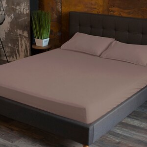 May include: A mauve fitted sheet on a dark gray bed frame with a tufted headboard. The bed is made with two matching pillowcases.