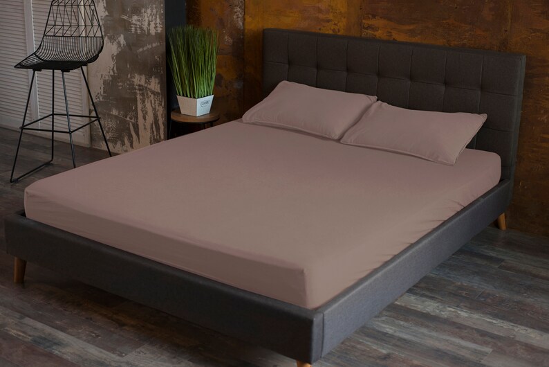 May include: A mauve fitted sheet on a dark gray bed frame with a tufted headboard. The bed is made with two matching pillowcases.