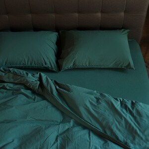 May include: A green bed with a white headboard and two pillows. The bed is made with a green duvet and a white sheet. The duvet is folded back to reveal the sheet.