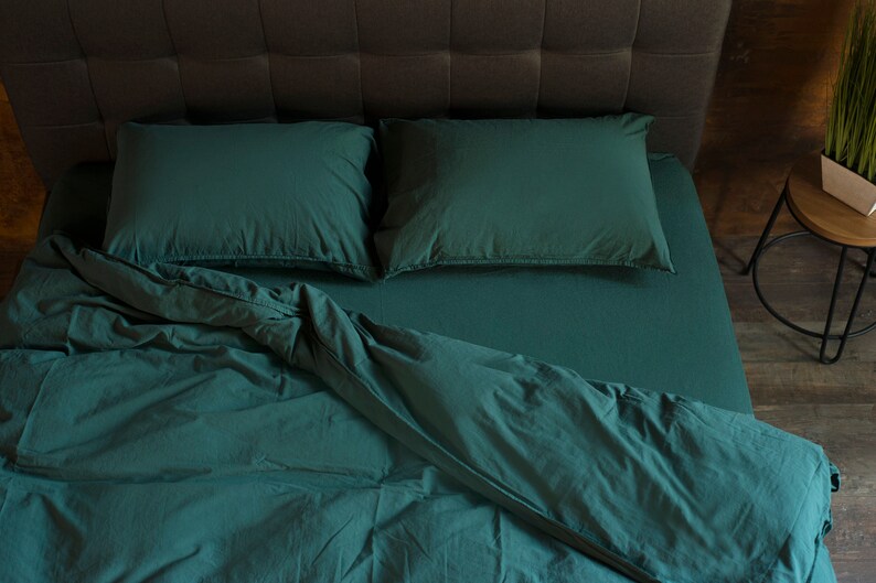 May include: A green bed with a white headboard and two pillows. The bed is made with a green duvet and a white sheet. The duvet is folded back to reveal the sheet.