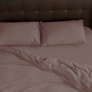 May include: A mauve colored bed with a duvet cover and two matching pillowcases. The bed is made with a soft, wrinkled fabric.