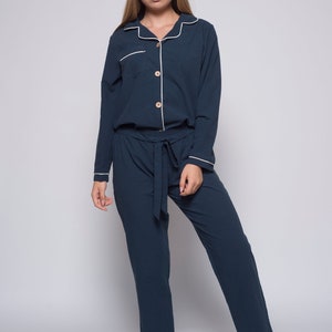 May include: A dark blue pajama set with white piping and a button-up top. The top has a chest pocket and a tie belt.
