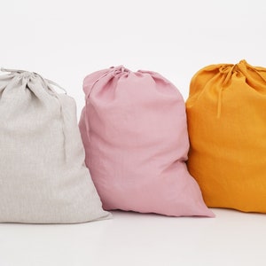 Può includere: Tre sacchi di lino con coulisse in diversi colori: grigio, rosa e giallo. I sacchi sono realizzati in un tessuto morbido e naturale e hanno un design semplice ed elegante.