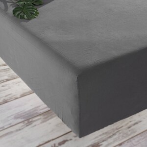 May include: A grey fitted sheet with a smooth, textured surface. The sheet is folded and displayed on a white wooden surface.