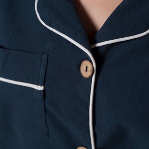 May include: A dark blue shirt with white piping around the collar and button placket. The shirt has a wooden button.