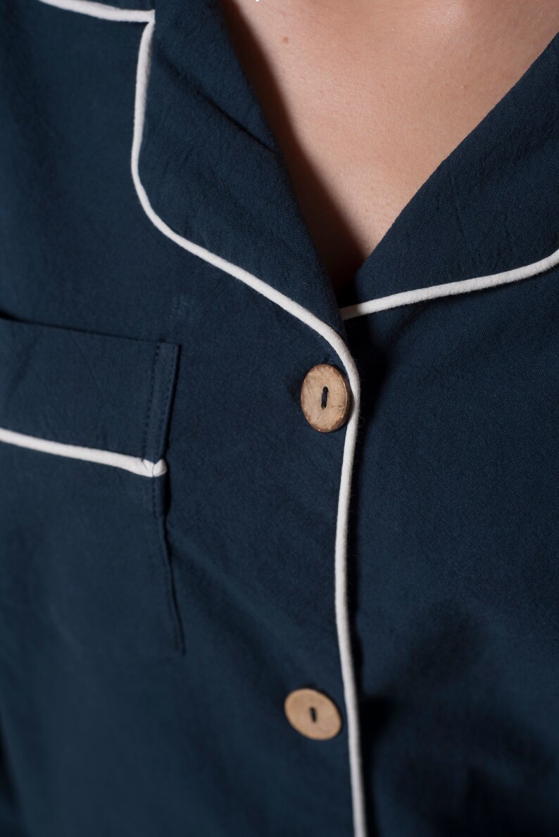 May include: A dark blue shirt with white piping around the collar and button placket. The shirt has a wooden button.