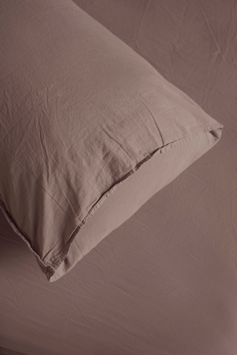 May include: A close-up of a soft, light brown pillowcase with a subtle texture. The fabric is smooth and appears to be made of cotton.