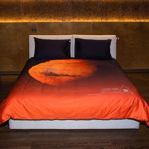 May include: A red and orange duvet cover with a graphic print of Mars, the planet. The duvet cover has a white text label that reads "ANDRE TAN".
