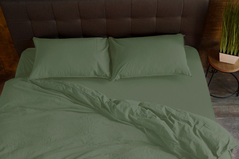 May include: A green bed with a white headboard and two green pillows. The bed is made with a green duvet cover and a white sheet.