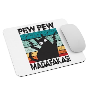 Puede incluir: Una alfombrilla de ratón blanca con un gato negro sosteniendo dos pistolas y un fondo retro de arcoíris. El texto "PEW PEW MADAFAKAS!" está impreso en la alfombrilla de ratón.