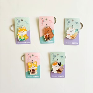 May include: Five keychains featuring cartoon animals with boba tea drinks. The animals include a Shiba Inu, bear, rabbit, Corgi, and cat. Each keychain has a silver ring and is attached to a card with Asian text.