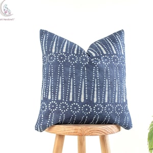 Puede incluir: Una almohada azul y blanca con un diseño geométrico. La almohada está sentada en un taburete de madera.