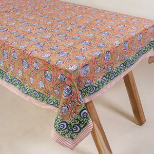 Op de afbeelding: Een koraalroze tafelkleed met een wit en blauw bloemenpatroon. Het tafelkleed heeft een groene en blauwe rand met een witte streep.