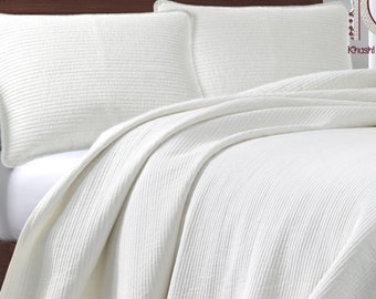 May include: White quilted bedspread with two white pillowcases. The bedspread has a subtle ribbed texture.