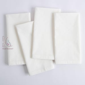 May include: Four folded white cloth napkins on a white background. The napkins are rectangular and made of a soft fabric. They are neatly folded, suggesting a formal dining setting. The napkins are clean and pristine.