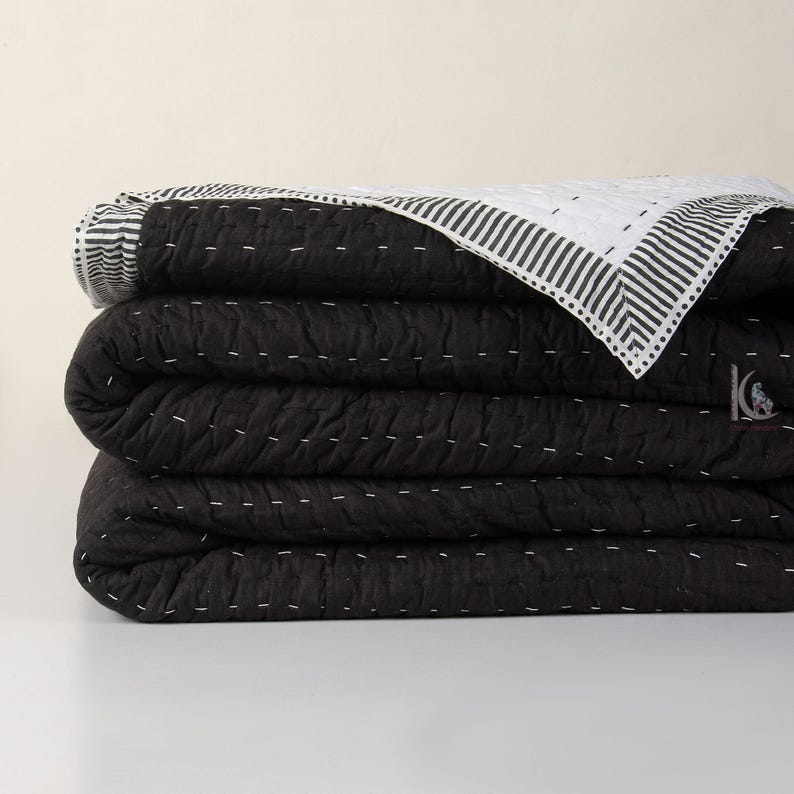 A solid black reversible Indian cotton Kantha quilt, showcasing its handstitched texture as a cozy winter blanket on a bed.