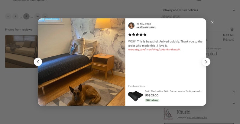 May include: A black and white kantha quilt with a natural design is displayed on a bed in a bedroom. The quilt is on a wooden bed frame with a brown dog lying on a gray and white patterned rug in front of the bed. The bedroom has a white wall with a floral wallpaper accent wall. A small wooden nightstand with a lamp is next to the bed.