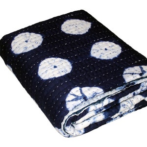 May include: A blue and white kantha quilt with a circular pattern. The quilt is folded and has a textured surface.