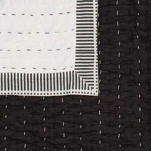 May include: A black and white quilt with a geometric design. The quilt features a white section with horizontal stitching and a black section with vertical stitching. The border has vertical stripes and dotted accents.