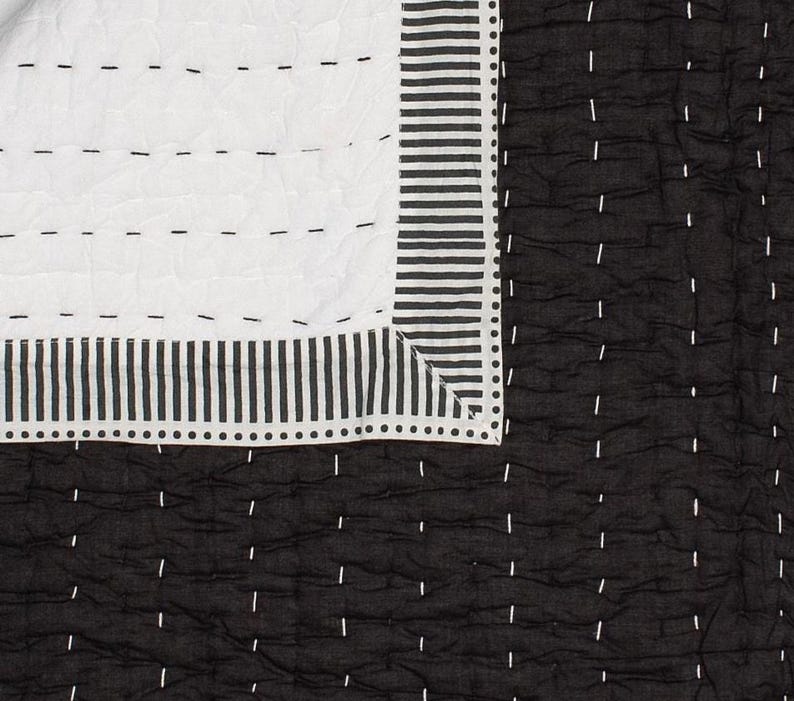 May include: A black and white quilt with a geometric design. The quilt features a white section with horizontal stitching and a black section with vertical stitching. The border has vertical stripes and dotted accents.