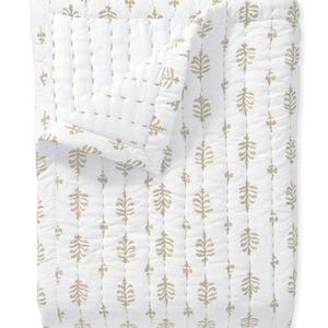 May include: White and beige quilted blanket with a repeating leaf pattern. The blanket is made of a soft material and has a stitched design. The leaf pattern is in a beige colour and is evenly spaced across the white background. The blanket is folded over.