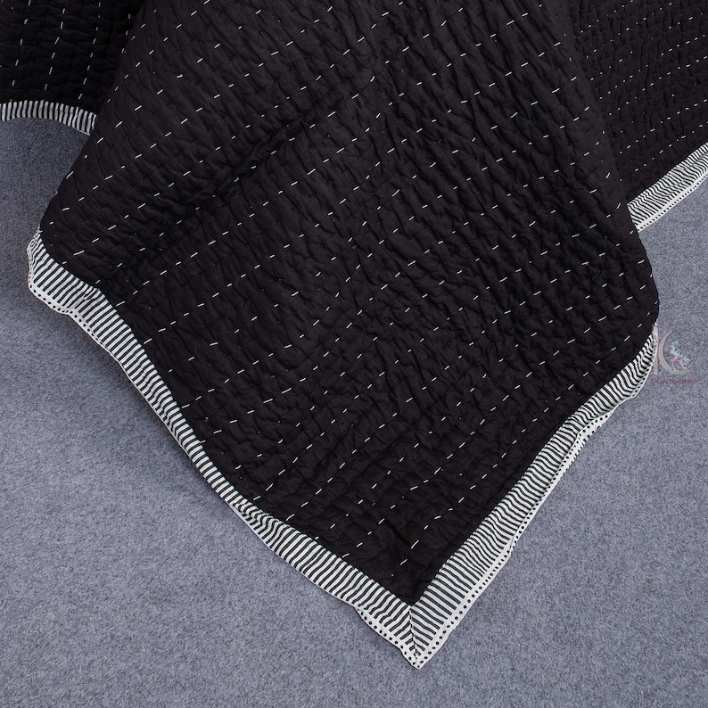 May include: Black quilted blanket with white stitching and a striped border. The blanket has a textured surface and a geometric pattern. The corner of the blanket is visible, showing the striped edge.