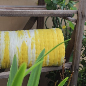 Op de afbeelding: Een gele en witte tie-dye stofrol op een houten plank. De stof is gevouwen en heeft een gestreept patroon.
