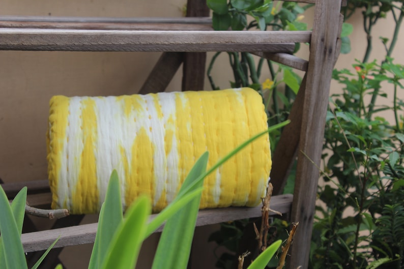 Op de afbeelding: Een gele en witte tie-dye stofrol op een houten plank. De stof is gevouwen en heeft een gestreept patroon.