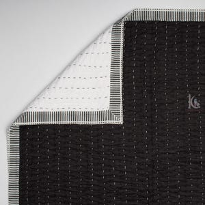 May include: Black and white quilt with a striped border. The quilt features a black fabric with white stitching and a white fabric on the reverse side. The border has a striped pattern. The quilt is folded to show both sides.