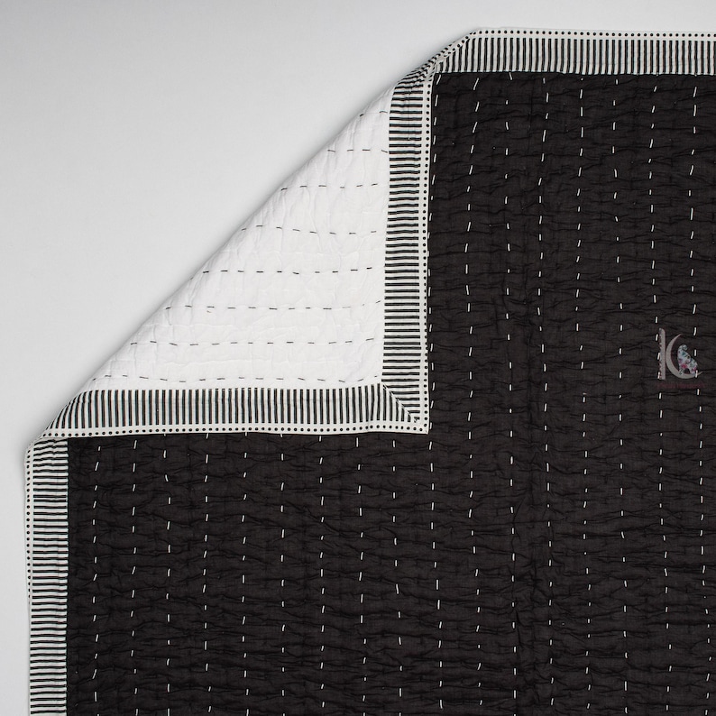 May include: Black and white quilt with a striped border. The quilt features a black fabric with white stitching and a white fabric on the reverse side. The border has a striped pattern. The quilt is folded to show both sides.