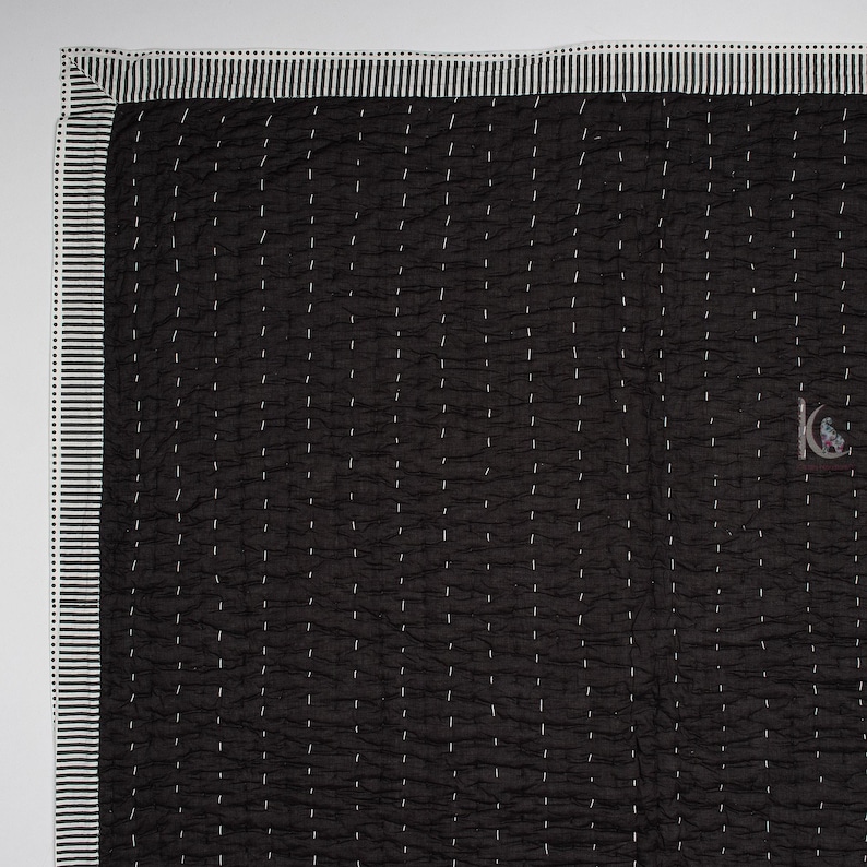 May include: Black quilted blanket with white stitching and a striped border. The blanket has a crinkled texture and a small logo in the bottom right corner. The border is white with black stripes.