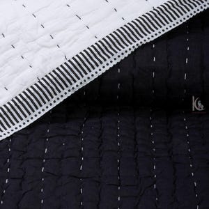 May include: A close-up of a black and white quilt. The quilt features a white top section with black stitching and a black bottom section with white stitching. The edge has a striped border with a dotted line.