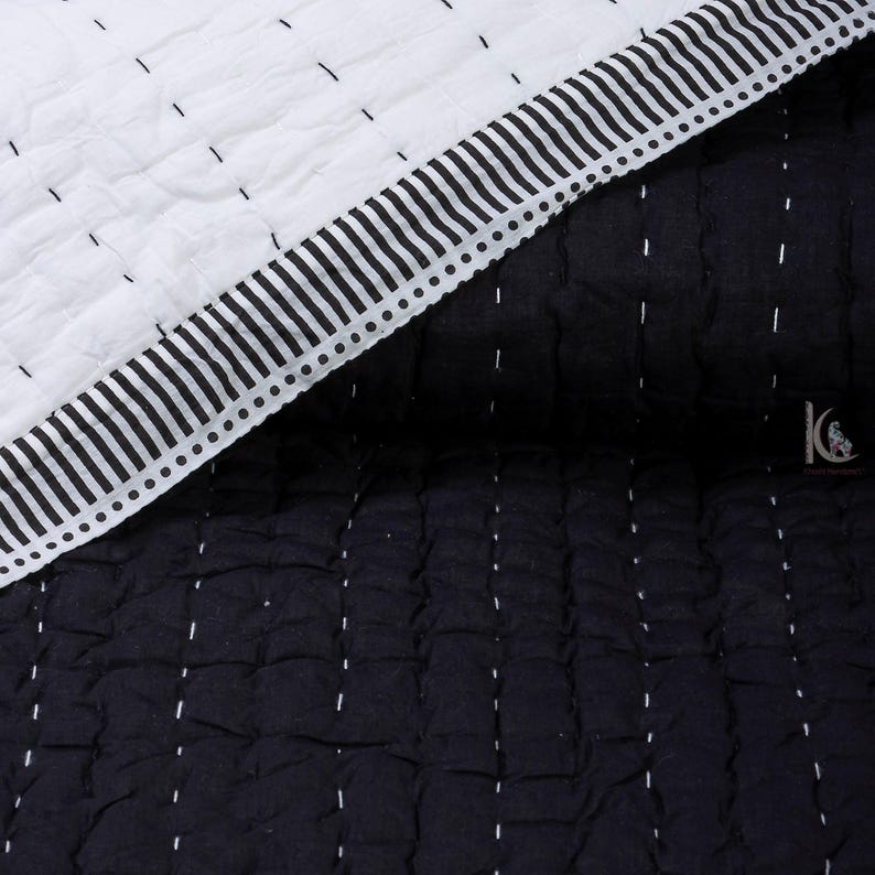 May include: A close-up of a black and white quilt. The quilt features a white top section with black stitching and a black bottom section with white stitching. The edge has a striped border with a dotted line.
