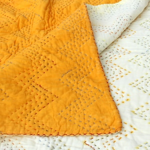 May include: A yellow kantha quilt with intricate hand-stitched patterns. The quilt is folded in half, revealing the white underside with a similar pattern.