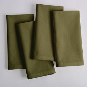 May include: Four olive green cloth napkins, folded and arranged on a white surface. The napkins are a solid color, with a slightly textured appearance. The napkins are a square shape and appear to be made of cotton or linen.