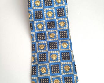May include: A blue silk tie with a repeating pattern of gold and black squares featuring a gold Medusa head design.