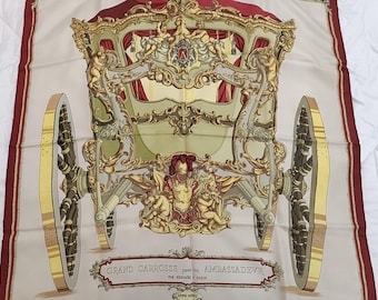 May include: A vintage silk scarf featuring a detailed illustration of a grand carriage with gold accents and a red and white interior. The text "GRAND CARROSSE pour l'AMBASSADEUR PAR HERMES A PARIS" is printed at the bottom of the scarf.