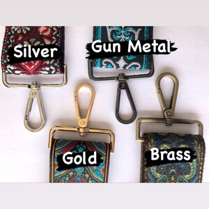May include: Four different coloured metal clasps for a bag strap. The clasps are silver, gun metal, gold, and brass. Each clasp is attached to a colourful patterned fabric strap.