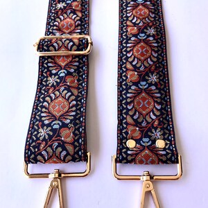 May include: A pair of black and gold adjustable straps with a floral pattern. The straps have gold clasps and metal rings.