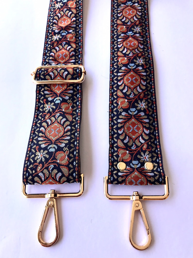 May include: A pair of black and gold adjustable straps with a floral pattern. The straps have gold clasps and metal rings.