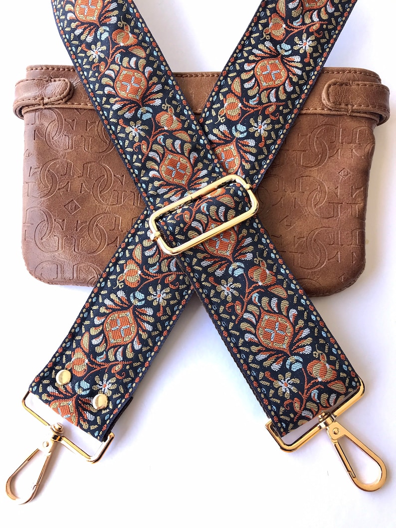 May include: A pair of black and gold adjustable straps with a floral pattern. The straps have gold clasps and are crossed over each other.