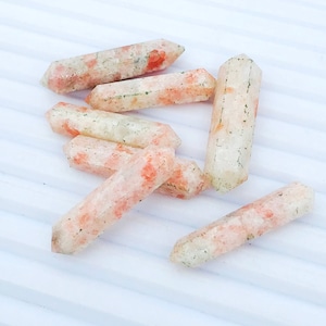 May include: A group of six sunstone points, each with a unique orange and white color pattern. The points are arranged in a random pattern on a white surface.